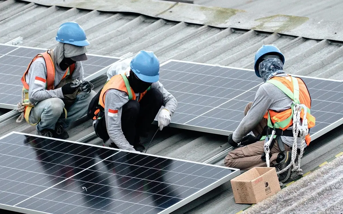 Three technicians fitting solar modules on the factory roof